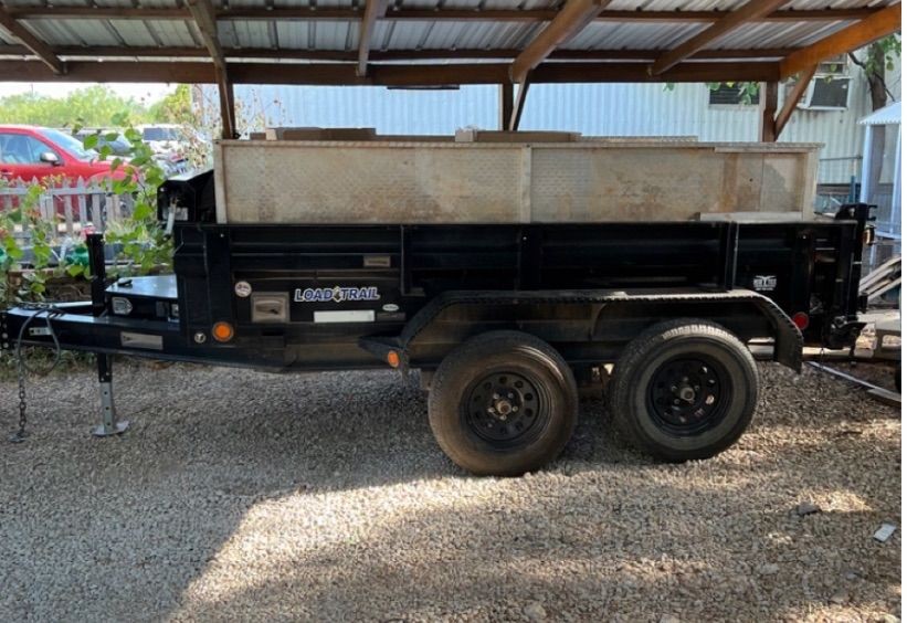 Black Load Trail utility trailer parked on gravel under a metal roof.