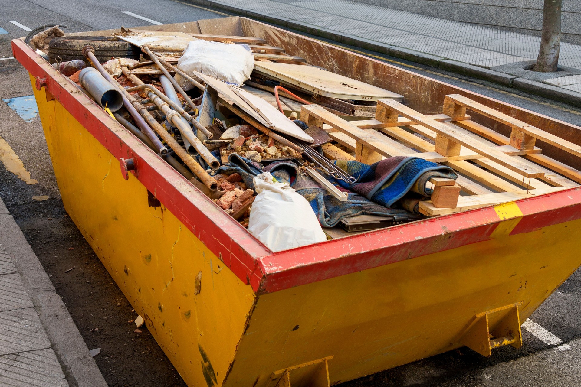 Yellow construction dumpster with a pile of debris and trash from the renovation